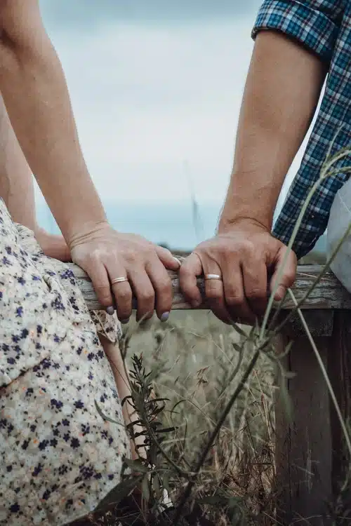 A couple's hands with wedding bands resting on wood.