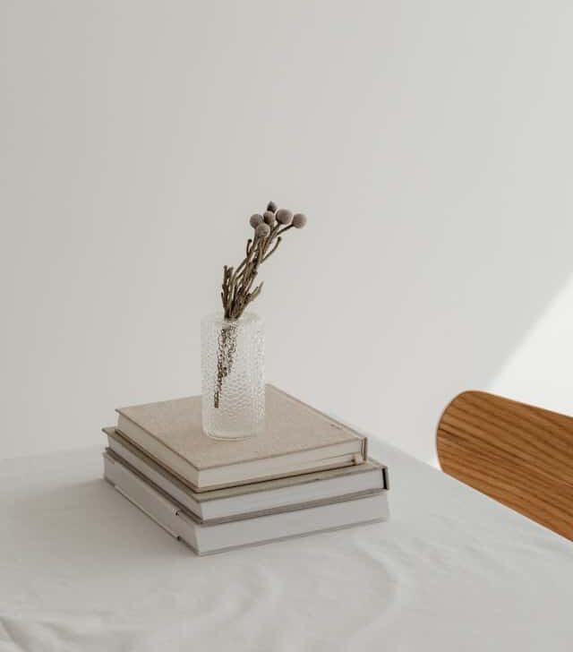 Stack of books with a small glass vase of dried flowers on top, warm still life in gentle natural light