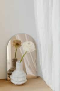 Flower arrangement reflected in a mirror against a white background, soft light enhancing balance and simplicity
