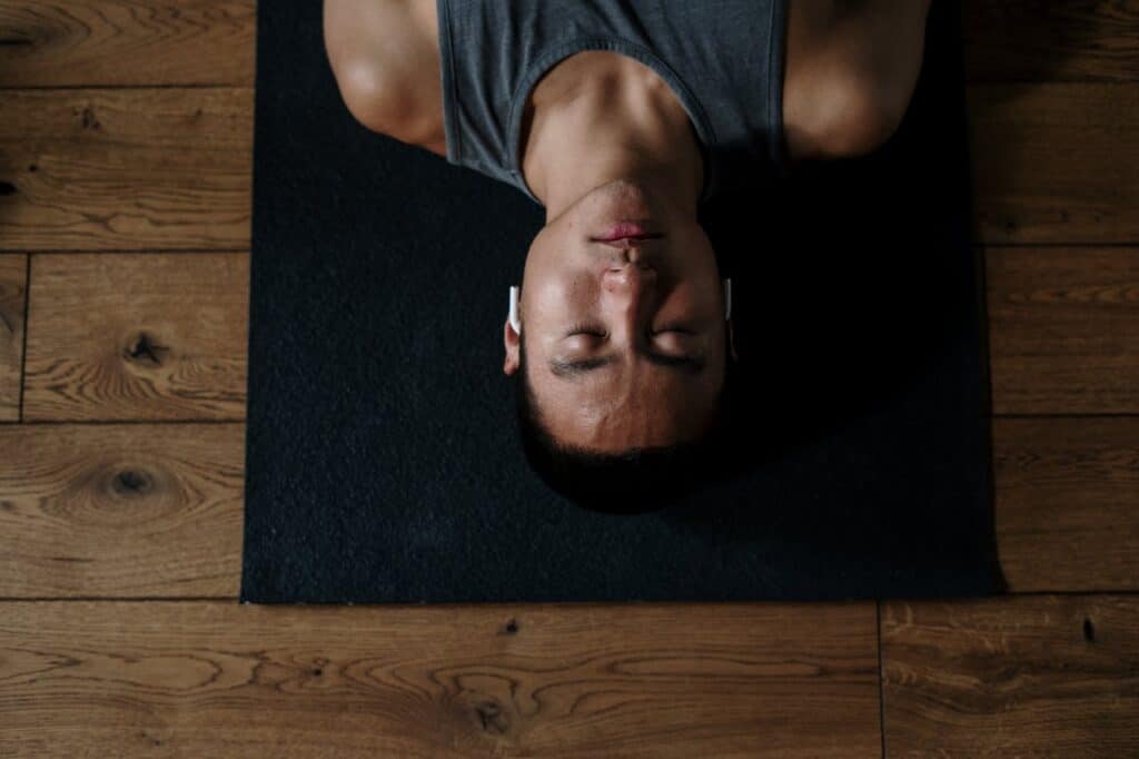 Person lying on a mat with eyes closed, practicing somatic therapy body awareness and grounding to calm the nervous system.