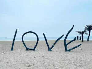 The word " love written in the sand on a beach with gentle waves nearby symbolizes romance, connection, and partnership