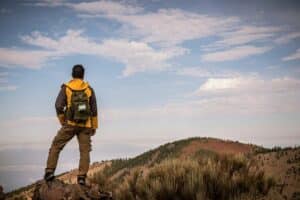 A lone man hiking on a mountain trail with a backpack, exploring the outdoors during a trekking adventure.
