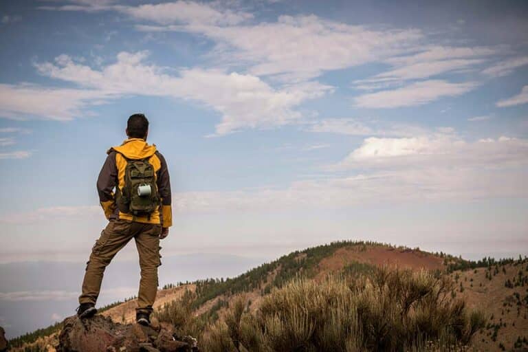A lone man hiking on a mountain trail with a backpack, exploring the outdoors during a trekking adventure.