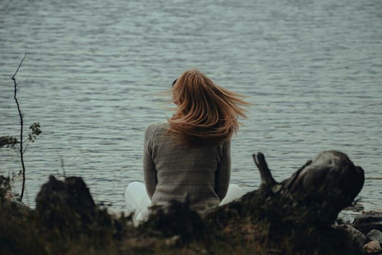 A woman sitting on the shore of a lake