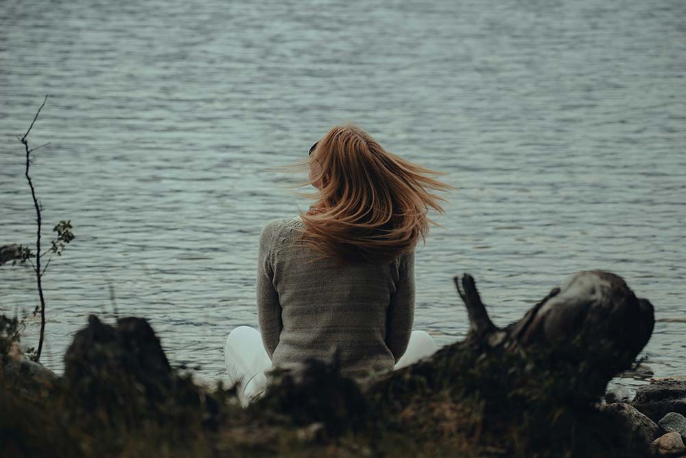A woman sitting on the shore of a lake