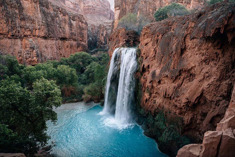 Waterfall cascading into a bright blue pool in a canyon