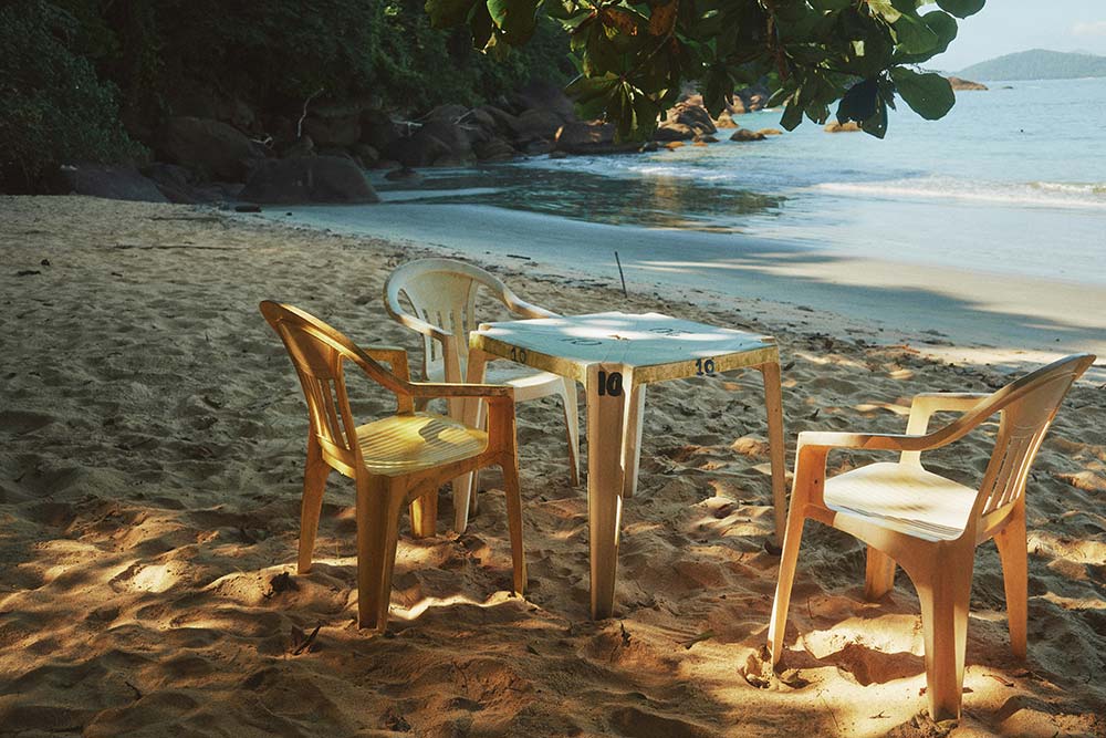 Table and chairs on a sandy beach under tree shade