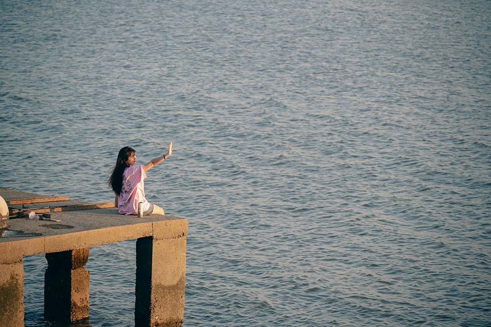 Girl sitting on a pier pointing at the water