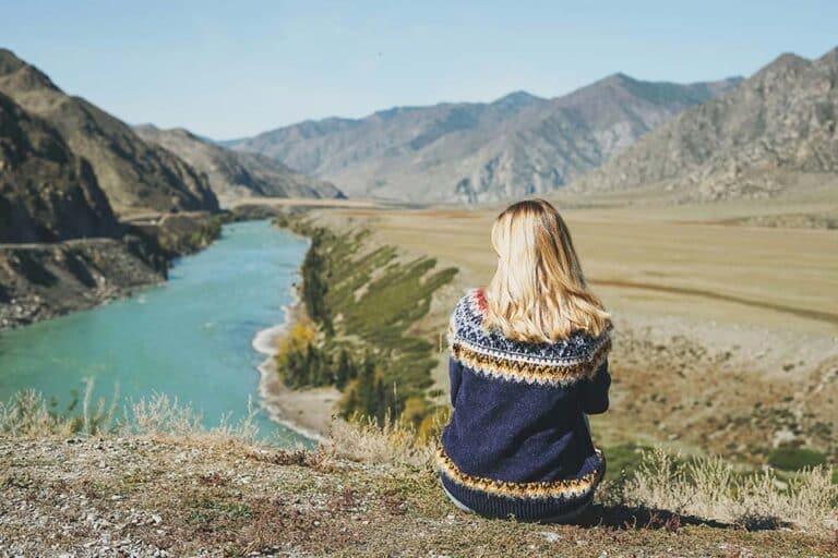 young blonde woman in nordic sweater sitting on background